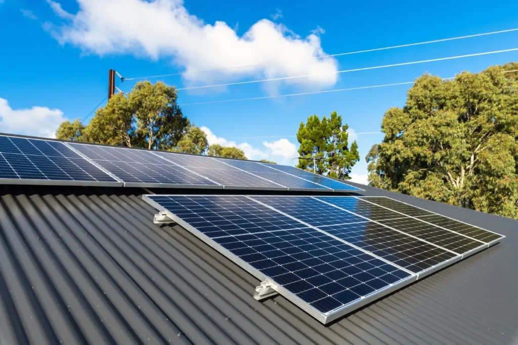 Instalación de paneles solares en el techo de una casa, con cielo despejado y árboles al fondo.