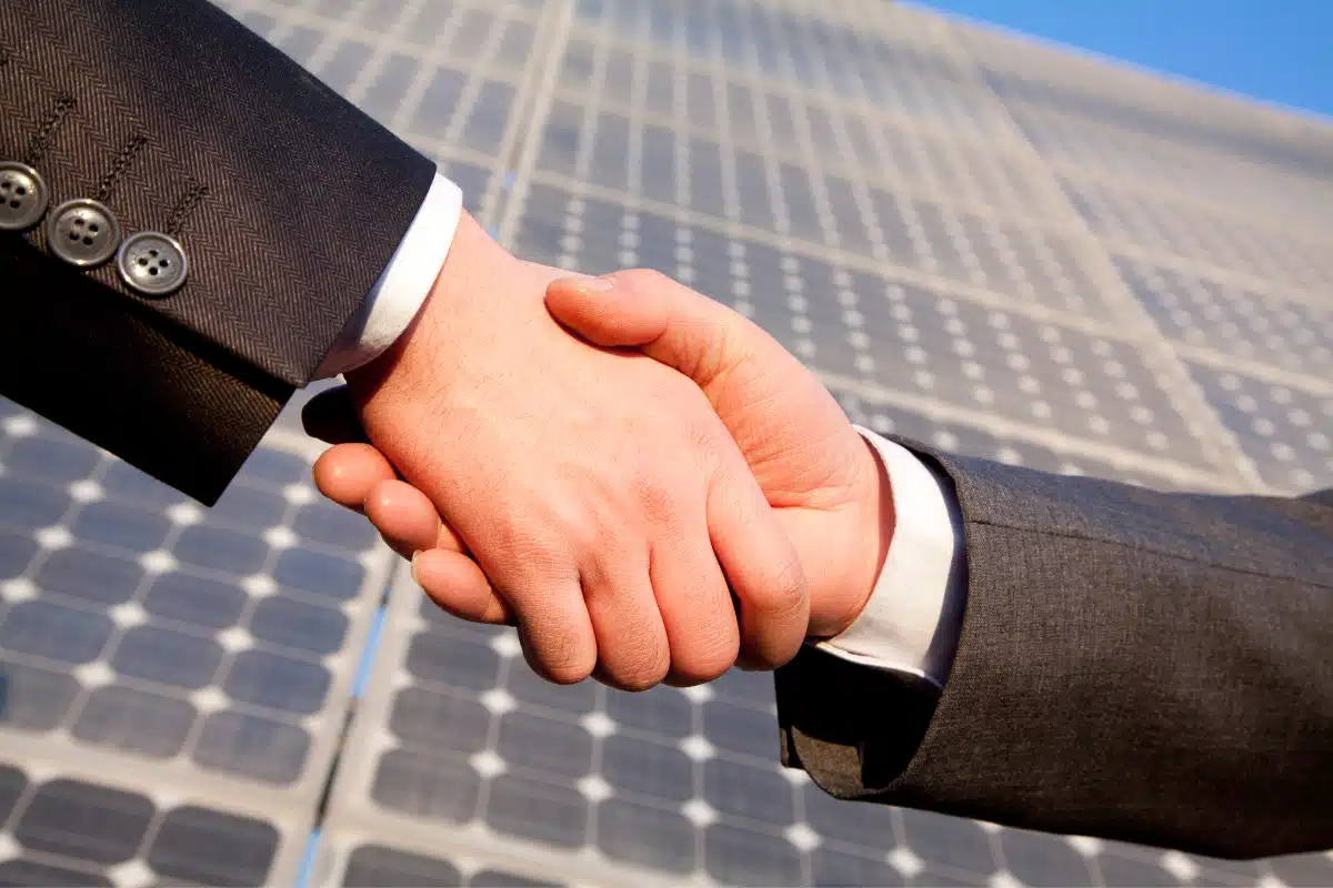 Dos empresarios estrechando la mano frente a paneles solares, ilustrando cómo la energía solar tiene ventajas competitivas para empresas