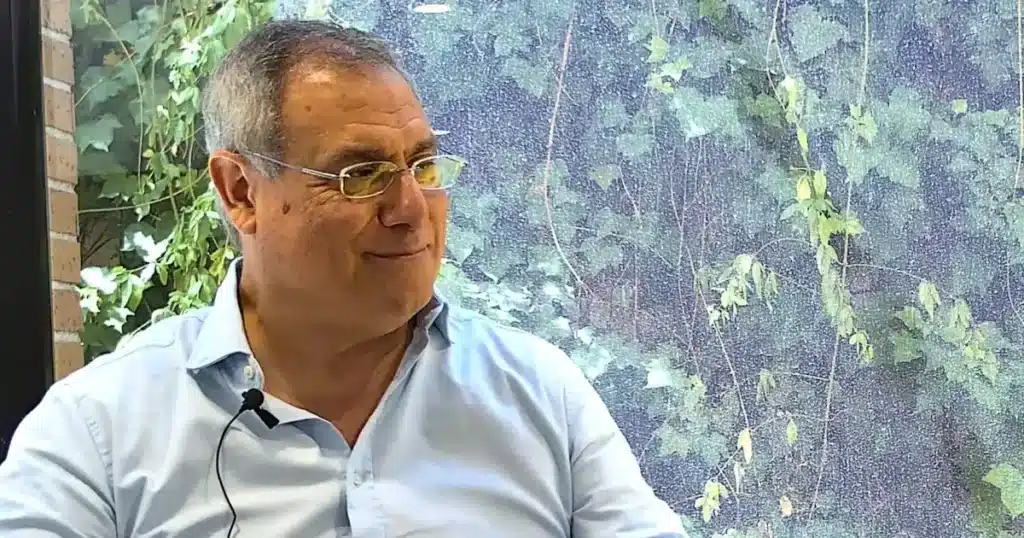 Luis Ortiz, Director Comercial de Perfecta Industrial (la división de Perfecta Energía dedicada a instalaciones solares industriales), en un entorno profesional, conversando mientras muestra una expresión amistosa y confiada; de fondo, se aprecia vegetación tras una ventana, transmitiendo calma y enfoque sostenible.