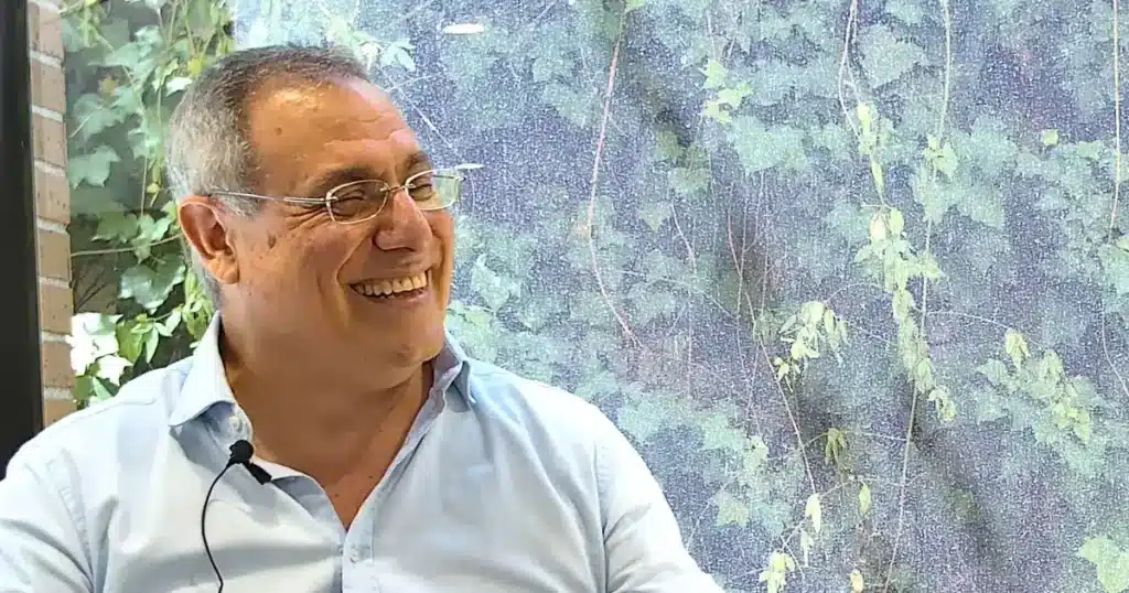 Director comercial de Perfecta Industrial en entrevista: gafas, sonrisa amplia y camisa azul; hojas verdes de fondo